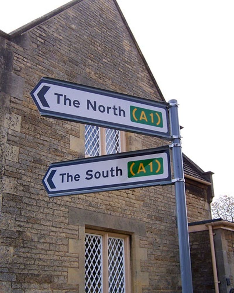 Photograph of a fingerpost type direction sign. The two fingers point roughly to the left, in only slightly different directions. One reads "The North (A1)" and the other "The South (A1)".