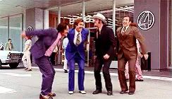 a group of men in suits and ties are dancing in front of a building with the number 4 on it .