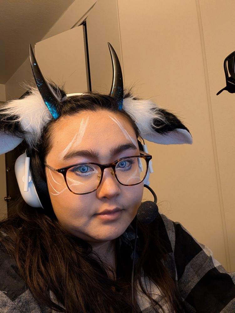 Selfie of egg with purple contacts and white and purple makeup. Dark horns, fluffy black and white ears, and a white headset. 