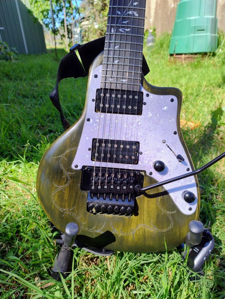 A green home finished 7 string electric guitar on a stand in the grass. Closeup of body.