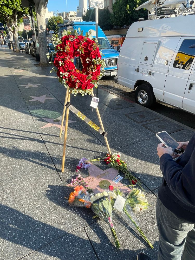 Photo of Rob Reiner’s star on the Hollywood Walk of Fame. A wreath of flowers has been placed there and the star is surrounded by bouquets of flowers laid on the ground.