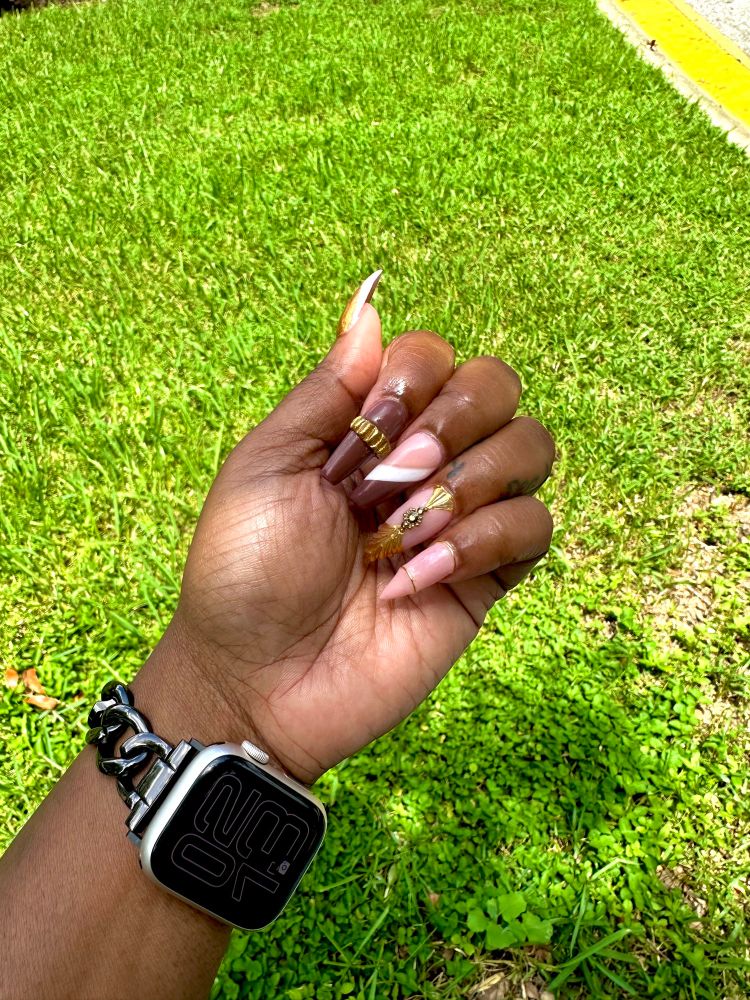 A mixture of stiletto and coffin shaped nails that are brown, nude and gold. 