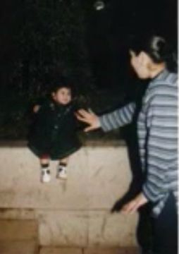 my mom wearing a long sleeve grey striped shirt holding her hand out for baby moni, wearing a black dress, to stay sat.