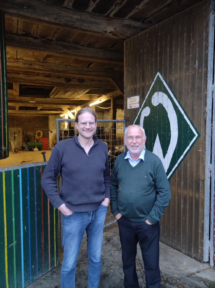 Bauer Willi und Bernhard Barkmann vor der Dielentür, die mit einem großen Werder-Emblem bemalt ist.