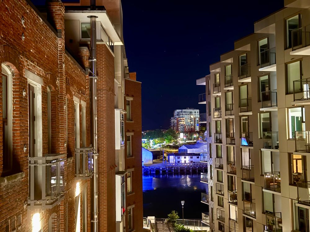 Picture of Victoria harbour taken at night between two long buildings. The blue reflection of the bridge illuminates the landscape