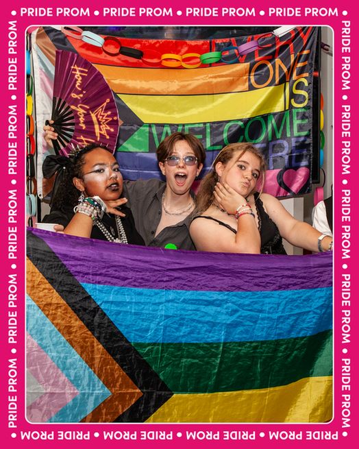 A photograph from Pride Prom last week, showing three young persons posing theatrically whilst holding a pride progress flag, and standing in front of another pride progress flag with the slogan ‘Everyone is Welcome Here’ emblazoned on it. The photograph is set in a border of Mosaic’s magenta brand colour, with ‘Pride Prom’ repeated around the edge. 