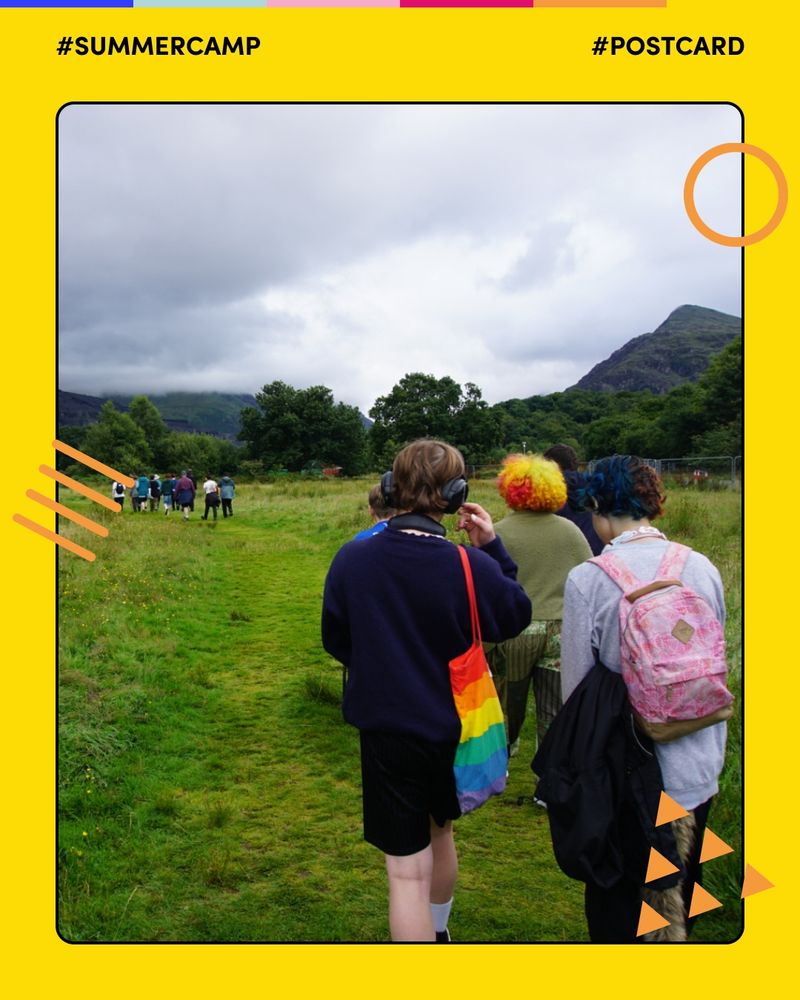 A group of young persons walk along a grassy trail surrounded by trees and hills under a cloudy sky. One young person in the foreground carries a rainbow tote bag and wears headphones. The photo has a yellow border with Mosaic’s orange graphic shapes, and includes the hashtags #SummerCamp and #Postcard.