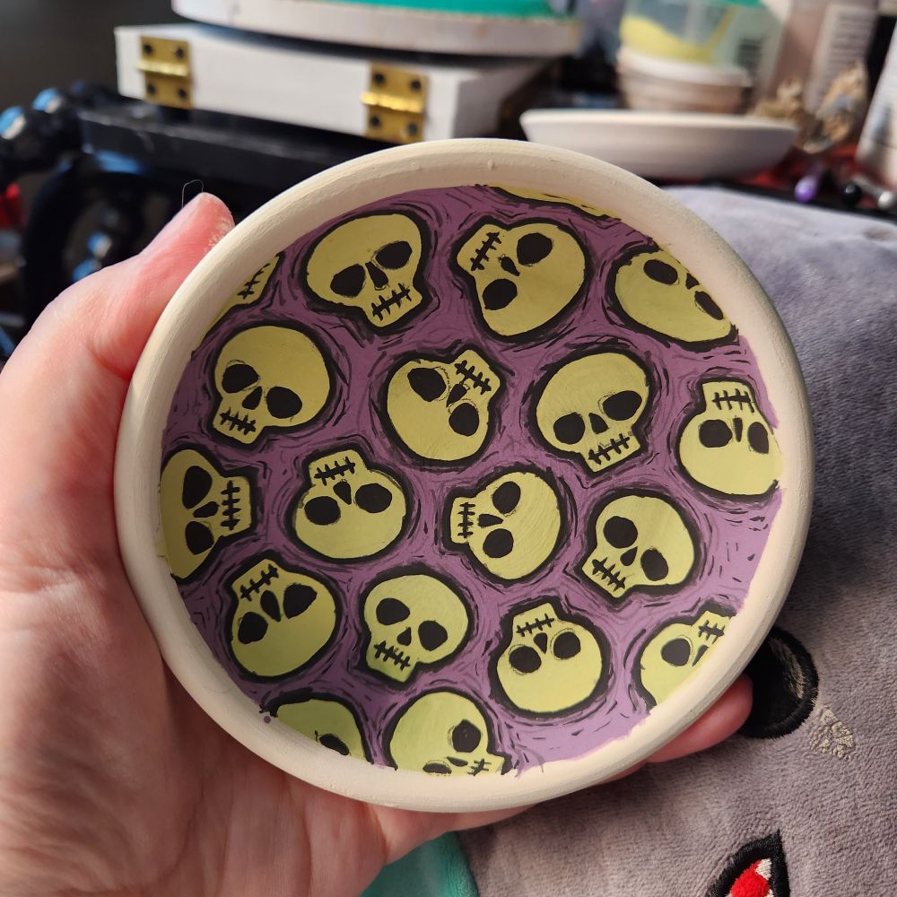 In progress painting of green skulls on purple background on low ceramic dish