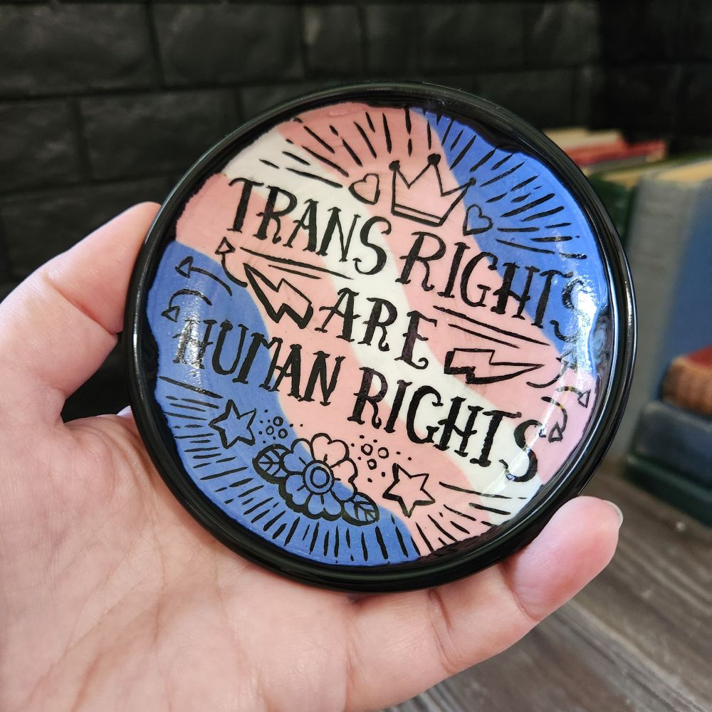 Finished trans rights are human rights trinket tray. Tattoo style text and tiny illustrations on a trans flag background 