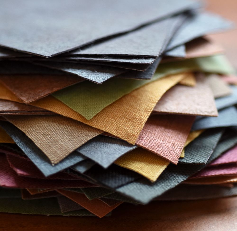 A stack of linen squares in shades of blue, pink, grey, yellow and green. Dyed with plants and ready to patchwork.
