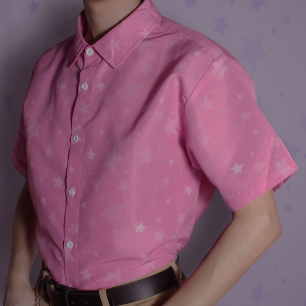 A short sleeve pink button up shirt tucked into pants, with a subtle star pattern covering it.