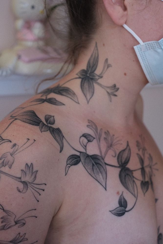 A close up view of the chest and shoulder section of the honeysuckle tattoo. The tattoo is black and grey with lots of negative space as the vine grows organically 