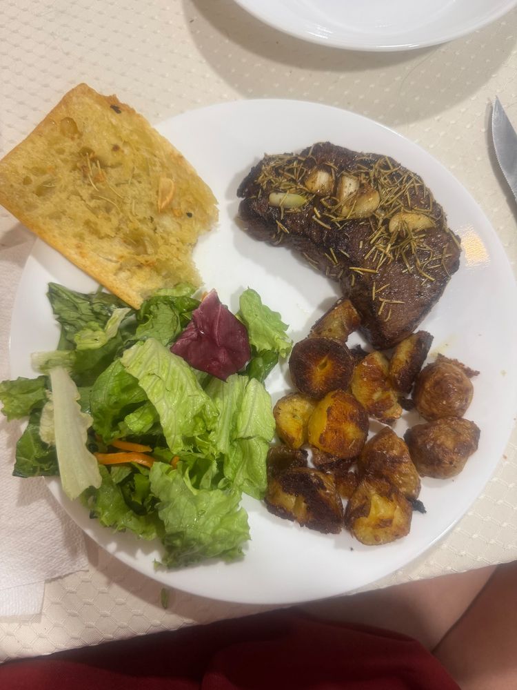 A photo of an impressive steak dinner including sirloin topped with rosemary and roasted garlic cloves, garlic ciabatta bread, salad, and well-crisped Yukon Gold potatoes.