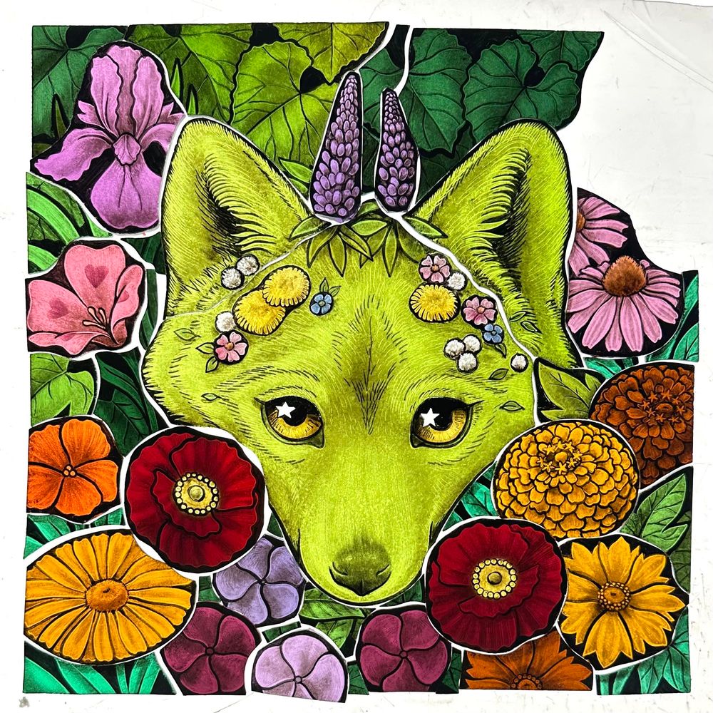 A green wolf face made of glass peeks from behind a bunch of beautiful wildflowers. Purple lupine grows from his forehead and dandelions and small flowers crest his brow. Marigolds, poppies, daisies, and other flowers gently frame his face. 