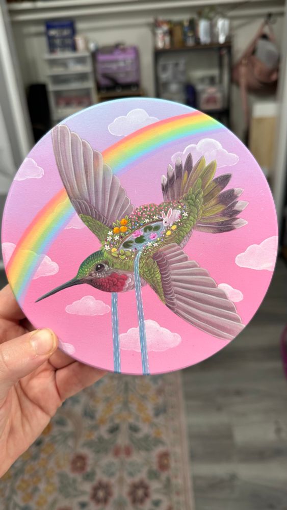 A bunny hops through a lush garden riding on the back of a blue and green hummingbird, zooming through a pink sky past a rainbow