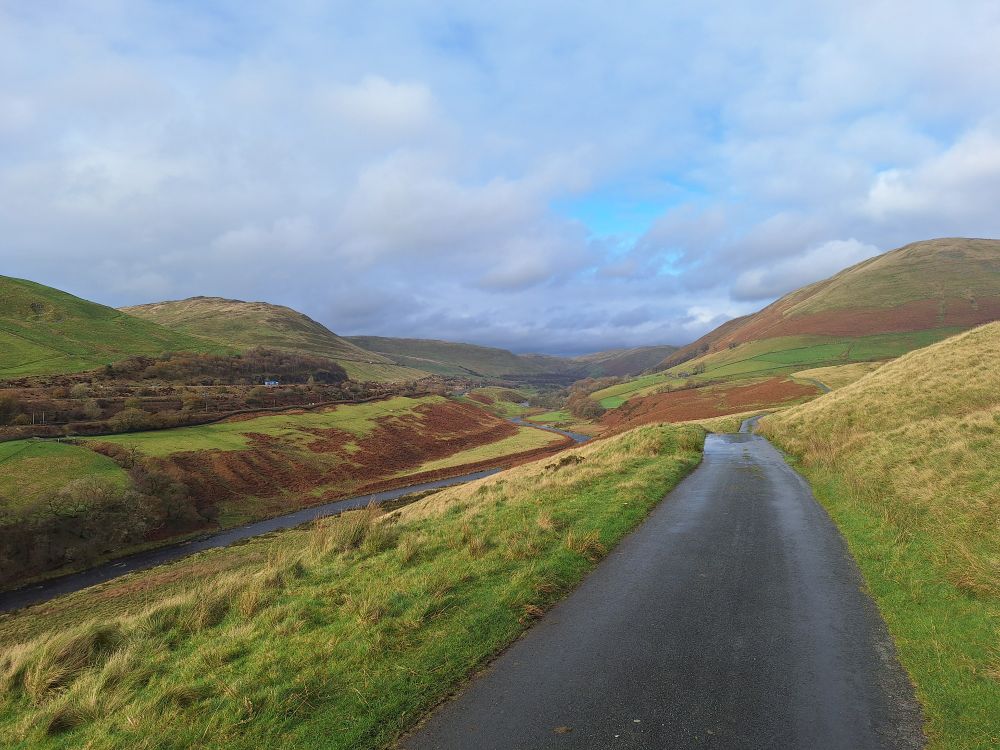 A deep river valley woth round green hills to either side. A road leads the eye towards  the gap in the hills.