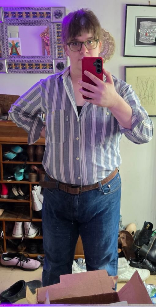 Picture of me with my hair up, in jeans and a blue-gray and white vertical striped button up shirt 