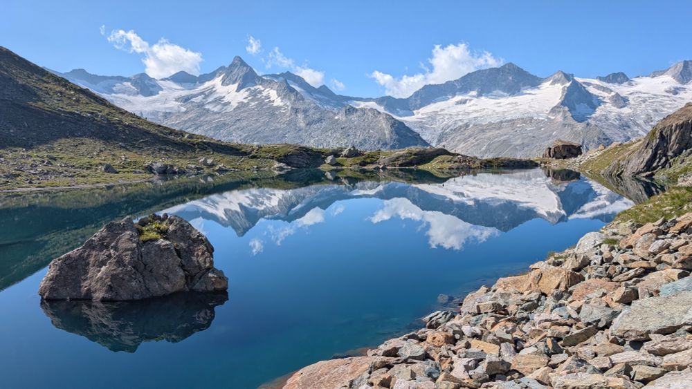 In einem blauen Bergsee spielen sich die dahinter liegenden vergletscherten Gipfel des Alpenhauptkamms 