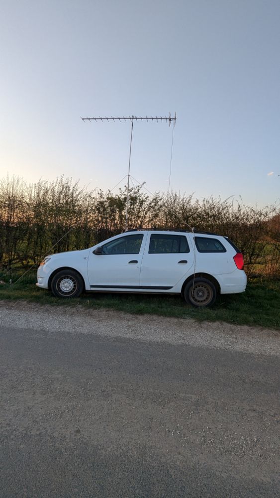 White car parked on grass verge next to single track road. With an 18 element 432 MHz beam on a 5 metre mast on the far side.