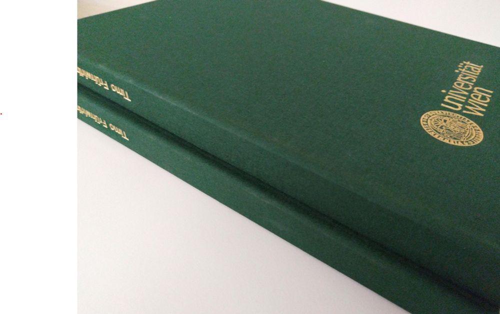 Two dark green hardcover books are stacked on top of each other.  The top book has "Universität Wien" and a gold circular seal embossed on its cover.  The spines of both books show the name "Timo Frühwirth" in gold lettering.