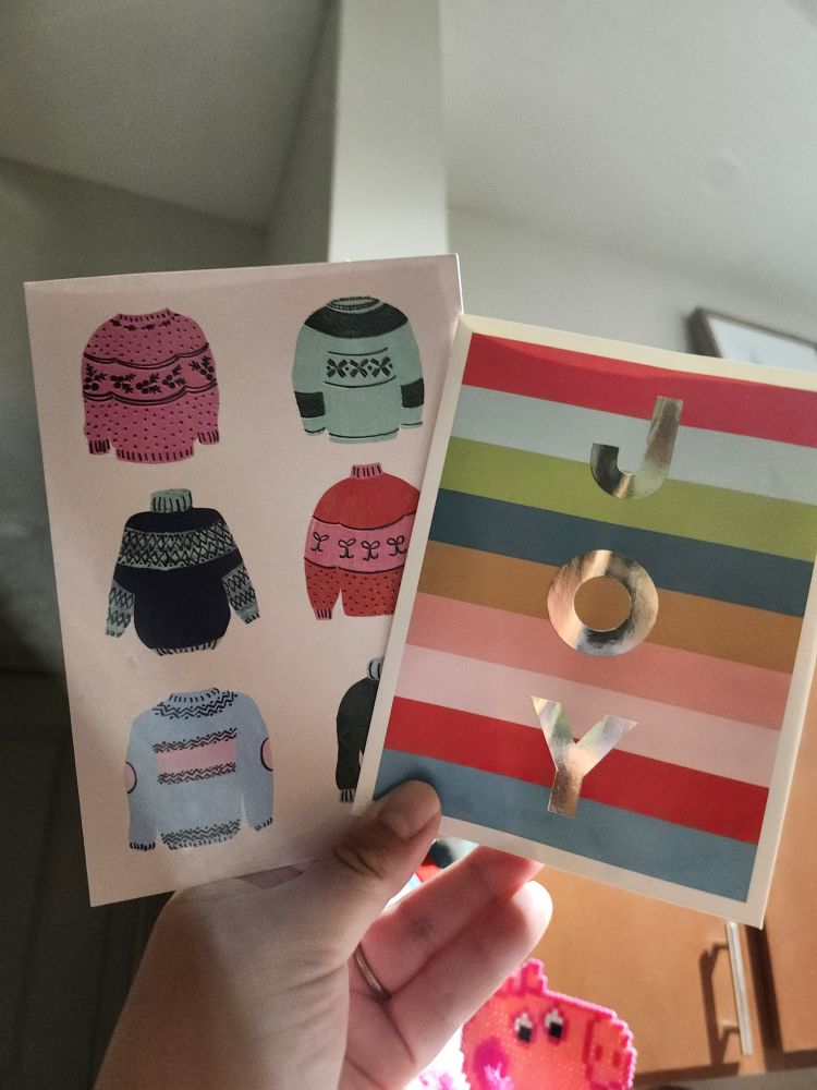 Two Christmas cards, the one on the left has different sweaters and the right has the word Joy on it