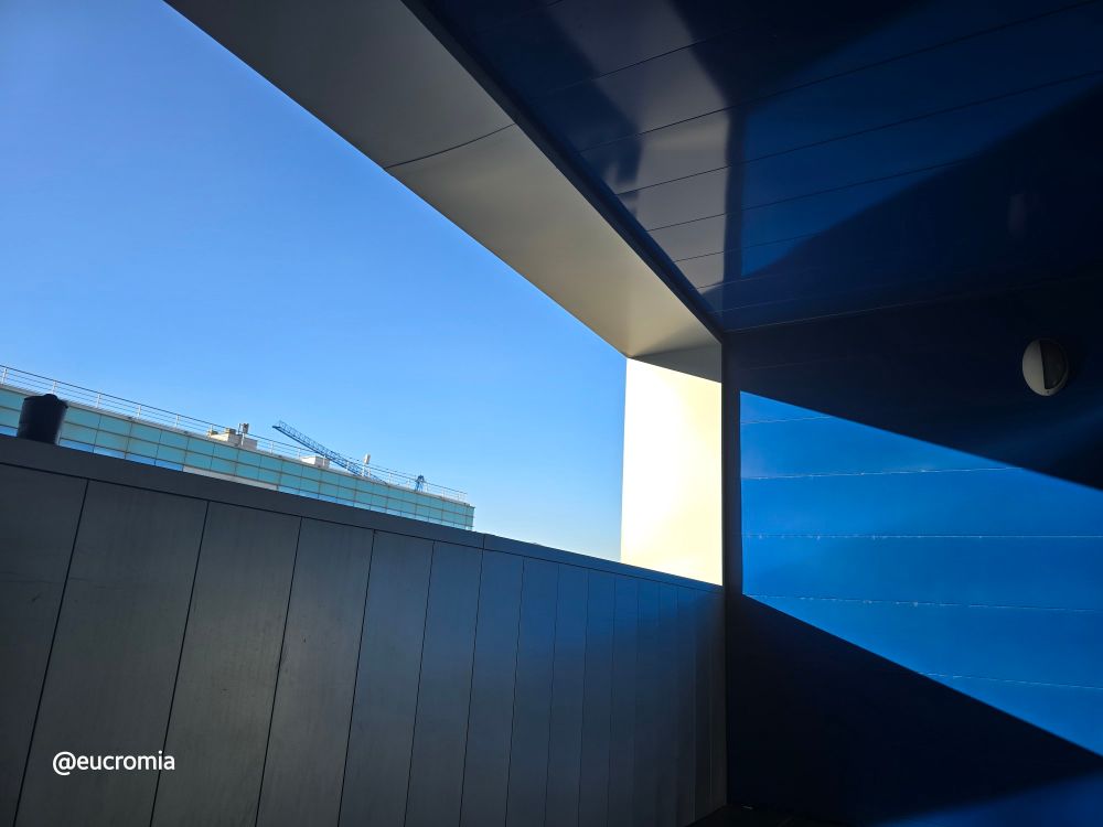 Foto da un balcone con parete azzurra e riflessi di cielo.