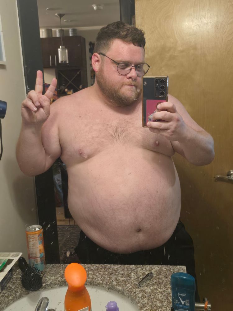Fat, shirtless man taking a mirror selfie while making a peace sign. 
