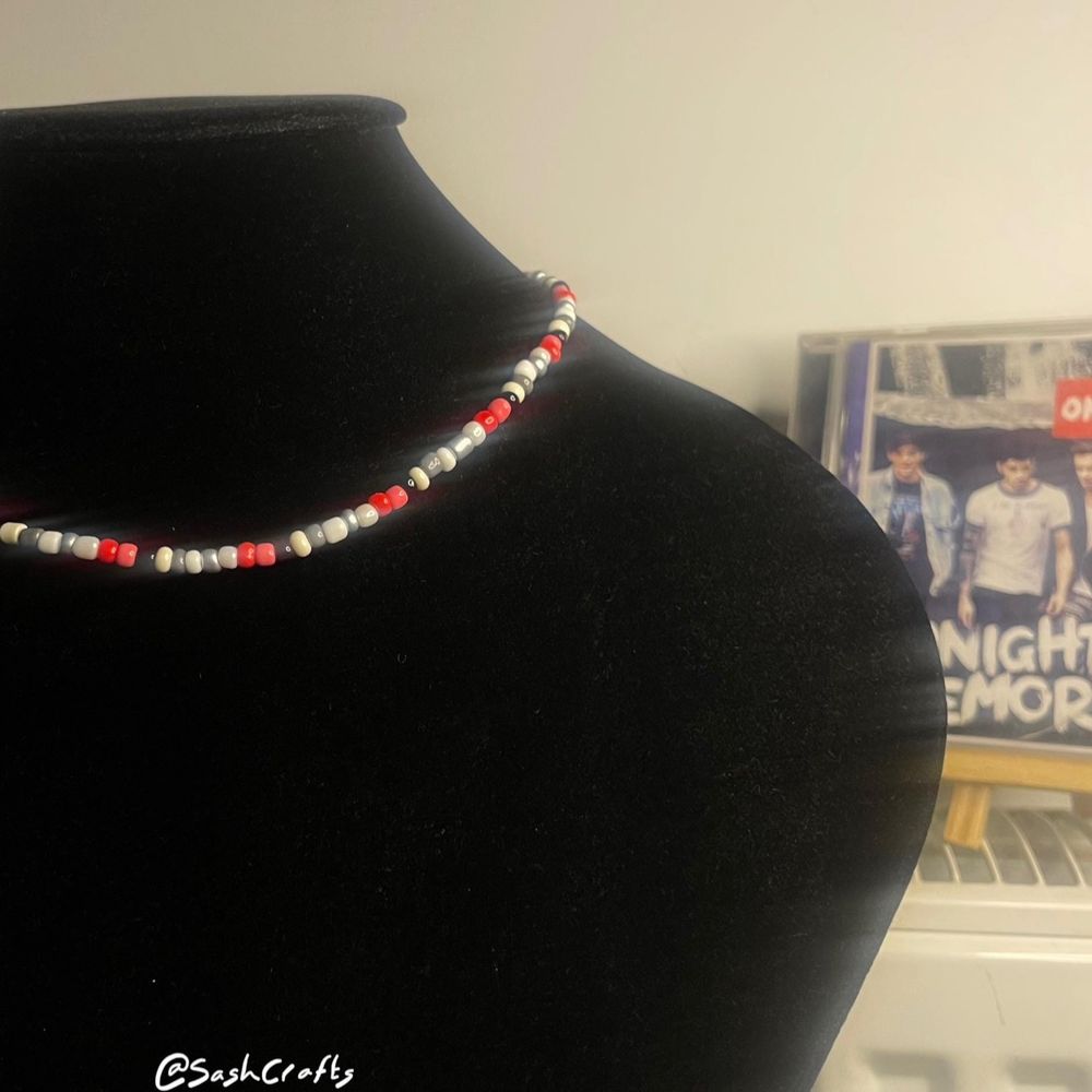 a large velvet black bust in the foreground, a small one in the back, both with matching jewellery on: necklace in front, bracelet in the back. one direction’s third album ‘midnight memories’, the colour inspo, is propped up in the bottom right. colours: black, reds, and white and greys/silver