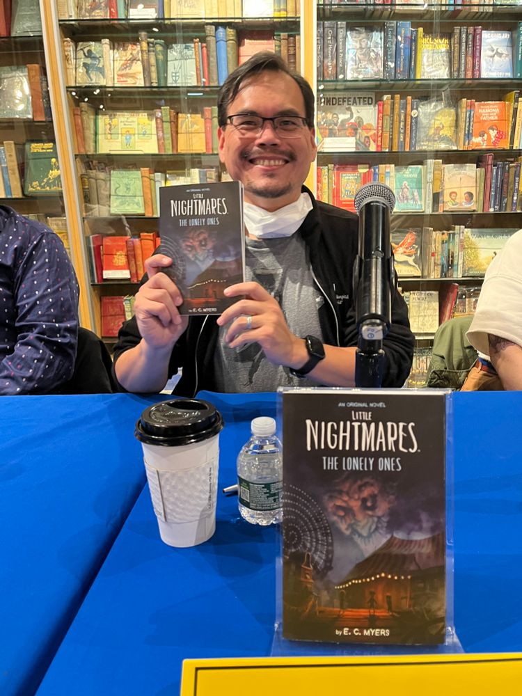 JAB author E.C. Myers sitting at a panel table at Books of Wonder and holding his new book, Little Nightmares: The Lonely Ones, with another copy displayed in front of him