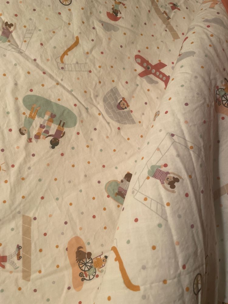 Photo of bedsheets: small colored polka dots on white background with colorful drawings of children playing. These are decidedly children’s sheets. On an adult’s bed