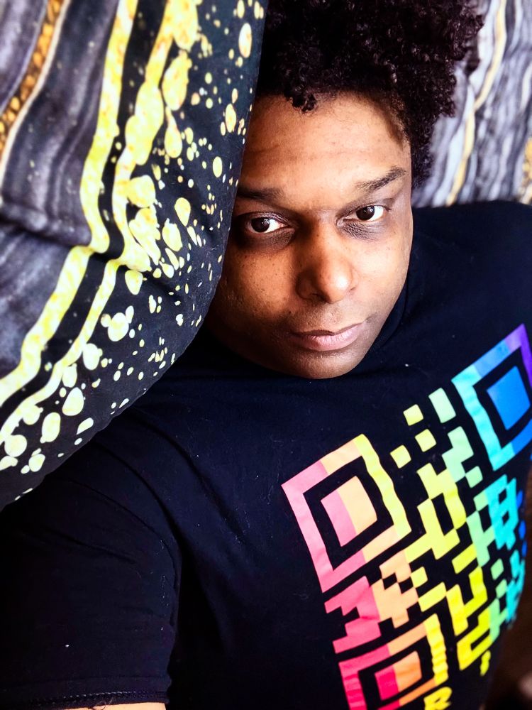 Picture of me wearing a black shirt with a gradient rainbow QR code on its center 