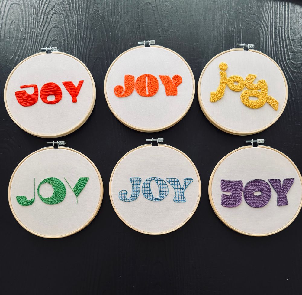 6 embroidery hoops. Each says Joy in a different font and color from the rainbow. 