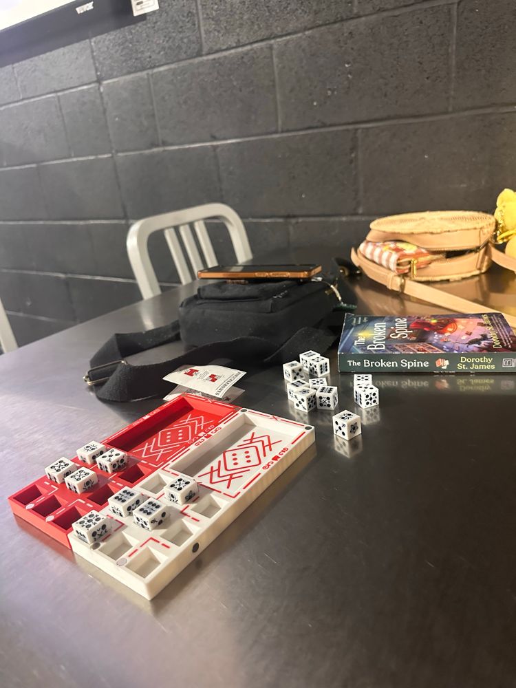 A metal table with a board game from cult of the lamb, a book, and purses on it