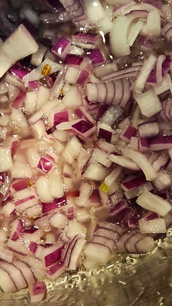 Diced red onions flecked with cumin seeds cooking in hot oil.