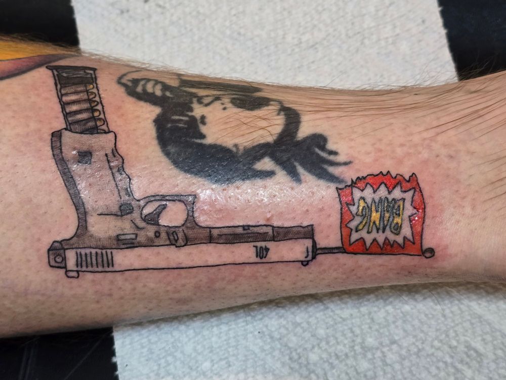 Pic of a fresh apprentice tattoo that features a glock, firing a cartoon BANG flag.
