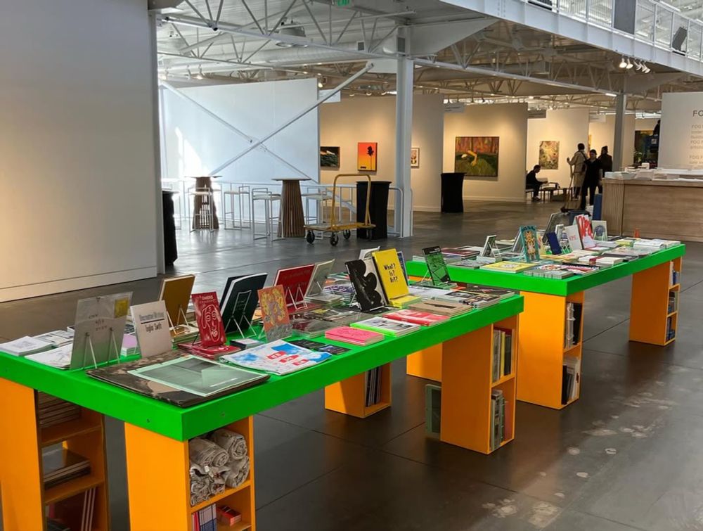 Books displayed on a bright green table in an art fair hall. 