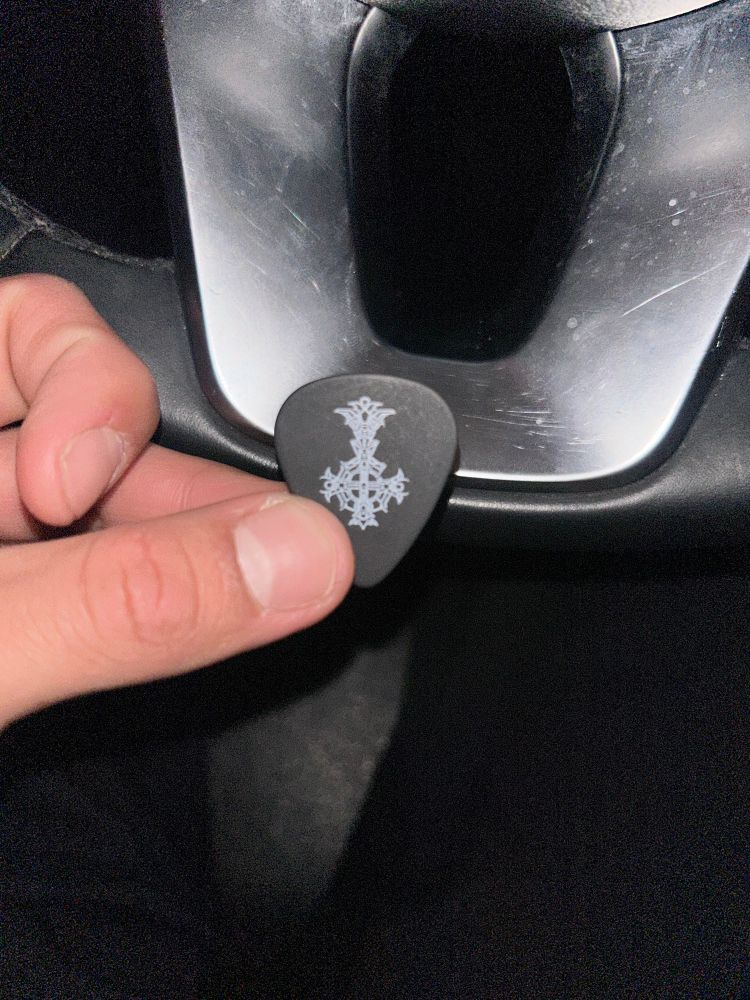 My left hand holding a black guitar pick with the Skeletá grucifix