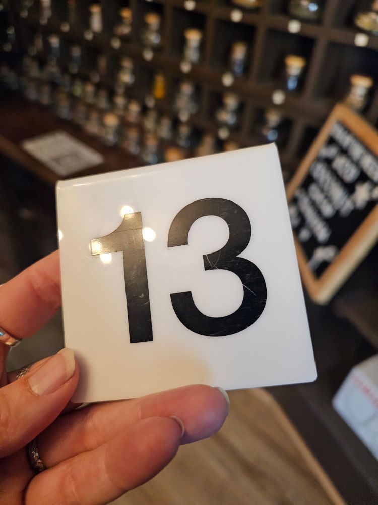 A number card with the nu.ber 13 in front of a wall of tea samples in an apothecary case. 