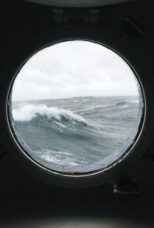 A porthole looking out on the ocean. The waves are grey, and the sky is overcast.