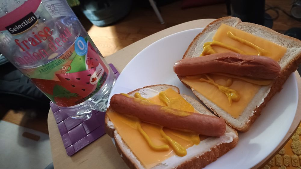 Hot dogs and mustard on white bread with cheese and mayo, and a bottle of strawberry and watermelon soda.