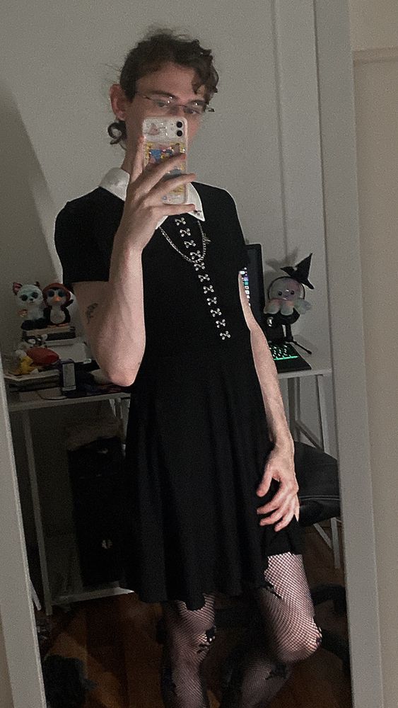 Boy (23) with short hair and glasses wearing a black collared dress and fishnets