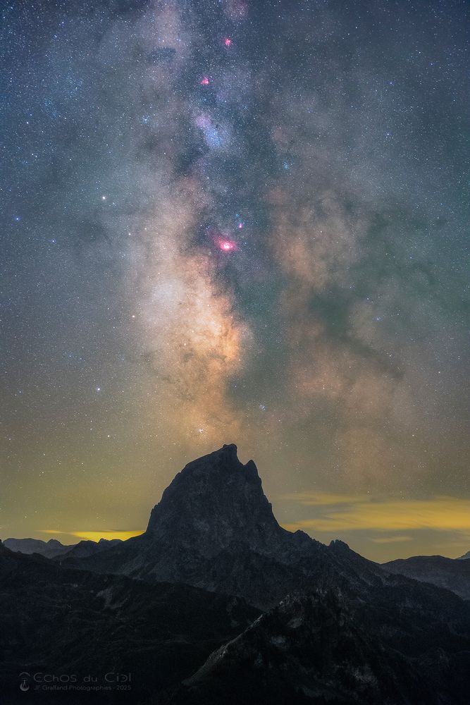 Le Pic du Midi d'Ossau, haut de 2884m, est un des plus hauts sommets des Pyrénées occidentales et semble s'élancer vers le ciel. J'avais imaginé depuis longtemps le capturer en pleine nuit accompagné de la Voie lactée, depuis un point de vue spectaculaire qui lui fait face.
Ici, la photo nocturne à longue pose révèle les détails et couleurs du cœur de la Voie lactée surplombant le Pic d'Ossau, avec notamment la tache rose de la nébuleuse de la Lagune, une zone active de formation d'étoiles dans notre galaxie.

The Pic du Midi d'Ossau, 2884m high, is one of the highest peaks in the western Pyrenees and seems to soar into the sky. I had long imagined capturing it at night, accompanied by the Milky Way, from a spectacular vantage point facing it.
Here, long exposure night photography reveals the details and colors of the heart of the Milky Way overhanging the Pic d'Ossau, including the pink spot of the Lagoon Nebula, an active star-forming zone in our galaxy.