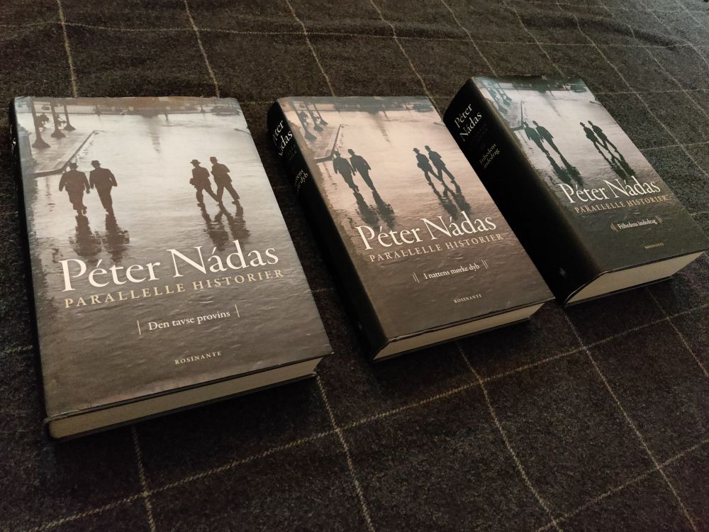 A picture of the three volumes of Péter Nádas' Parallel Stories. Each volume shares the same cover art, with two separate duos of men walking together, but with a minor difference in hue.