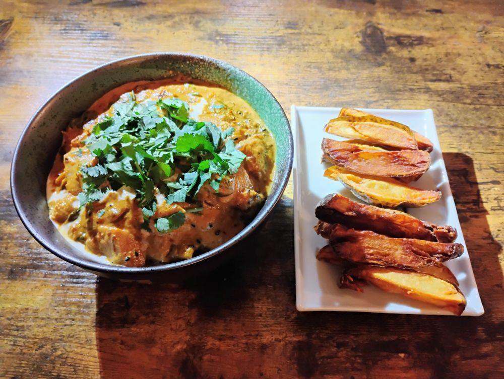 A bowl of curry with cilantro on top, next to a plate of fried potatoes.