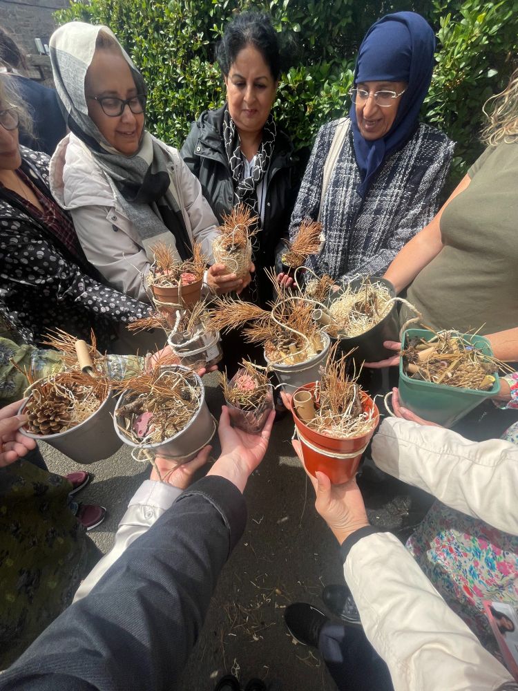 A group of people stand in a circle with their hands in the centre holding mini bug hotels.