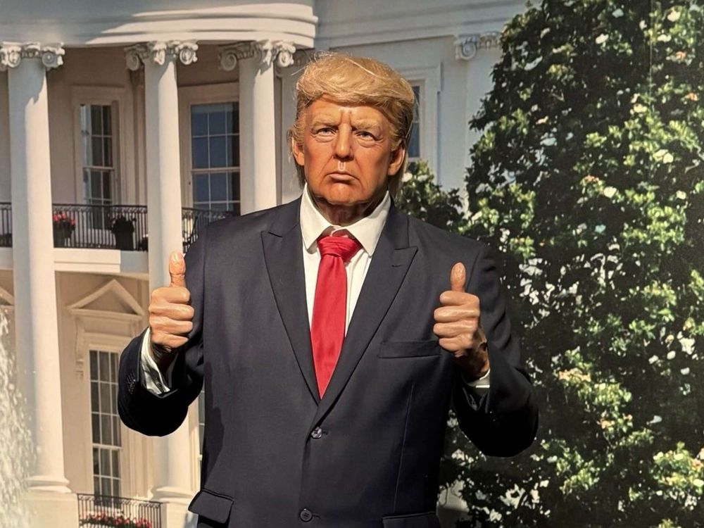 wax statue of trump with two thumbs up in a suite and red tie 
