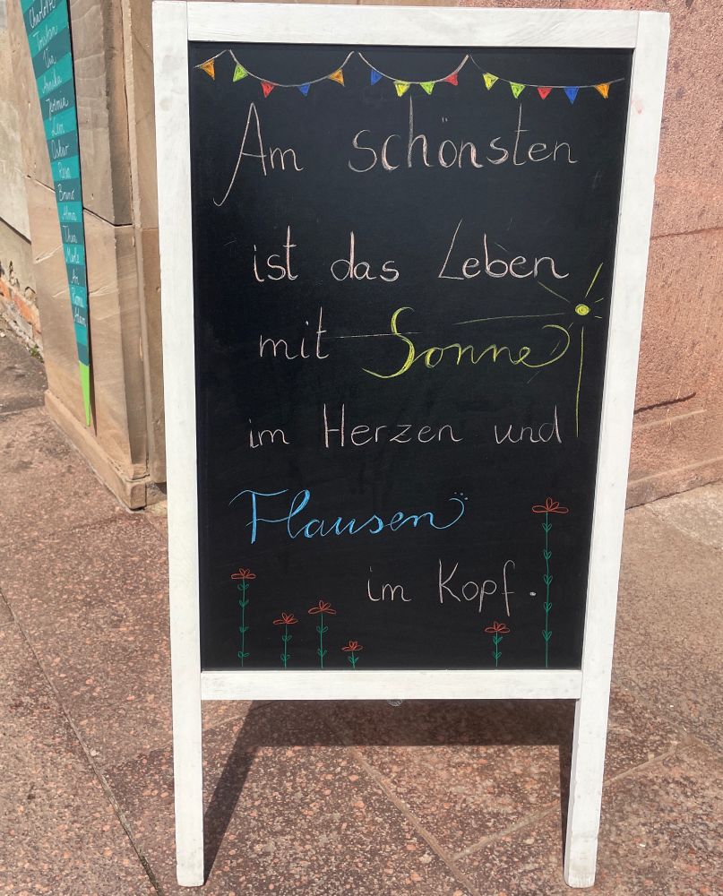 Das Bild zeigt eine Tafel mit der Aufschrift "Am schönsten ist das Leben mit Sonne im Herzen und Flausen im Kopf"

