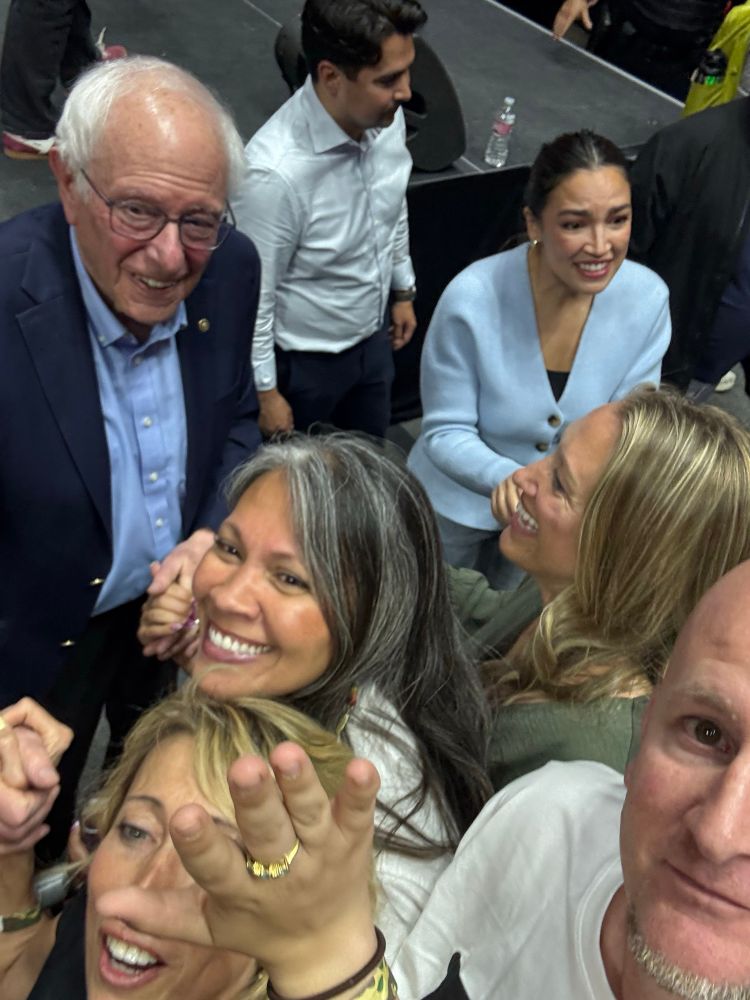 A group of people taking selfies with Sen. Bernie Sanders and Rep. Alexandria Ocasio-Cortez. 