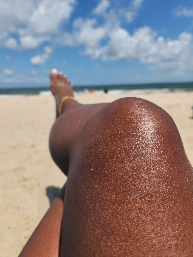 A brown crossed leg and foot goes out of focus into an unfocused shore/sky view