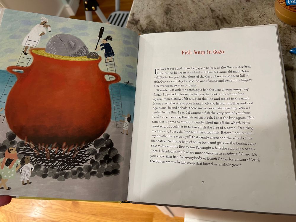 Picture of a book opened to a page that says “Fish Soup in Gaza,” with a colorful illustration of a giant soup pot with a giant fish inside, resting on hot coals on the beach.